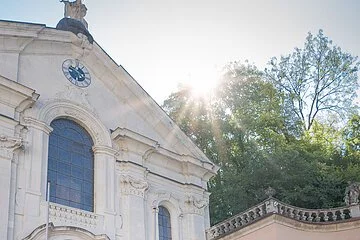 Zwei Frauen und ein Mann stehen vor der Kirche im Klosterinnenhof und bestaunen das Gebäude von außen.